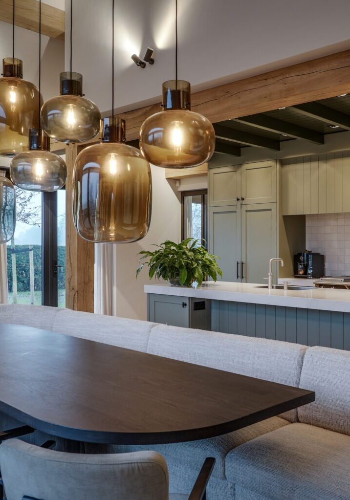Glazen hanglampen boven eettafel met bankstel en landelijke keuken op de achtergrond