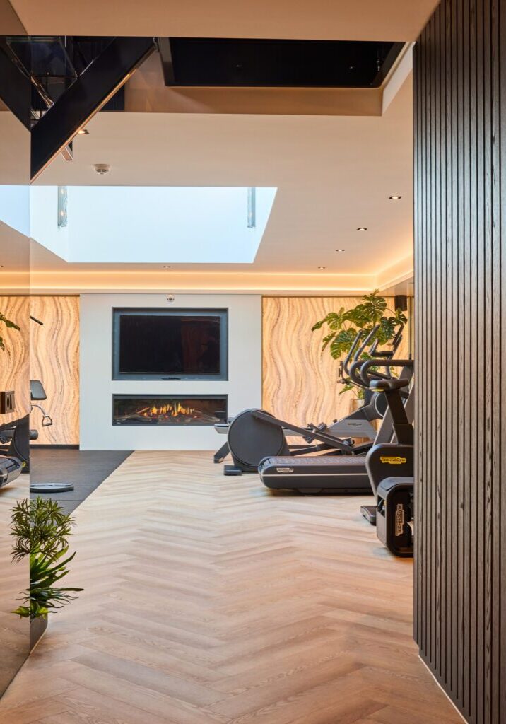 Doorkijk in privé gym met spiegelwand, lamelwand in donker eiken en ingebouwde haard