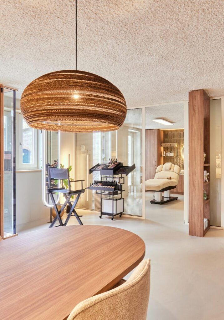 Overzicht ontvangstruimte schoonheidssalon Sqin — ronde tafel, kartonnen hanglampen, balie en doorzicht naar behandelkamers