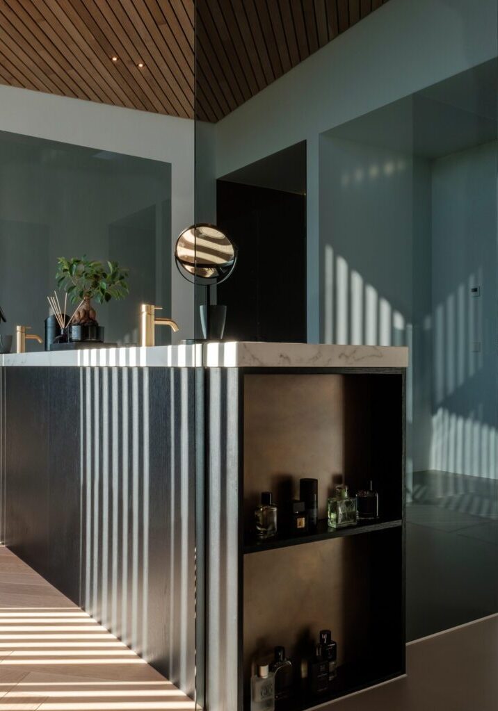 Badkamer met donker badmeubel, marmeren blad en messing kranen achter glazen wand – interieurbouw Mint Interieur